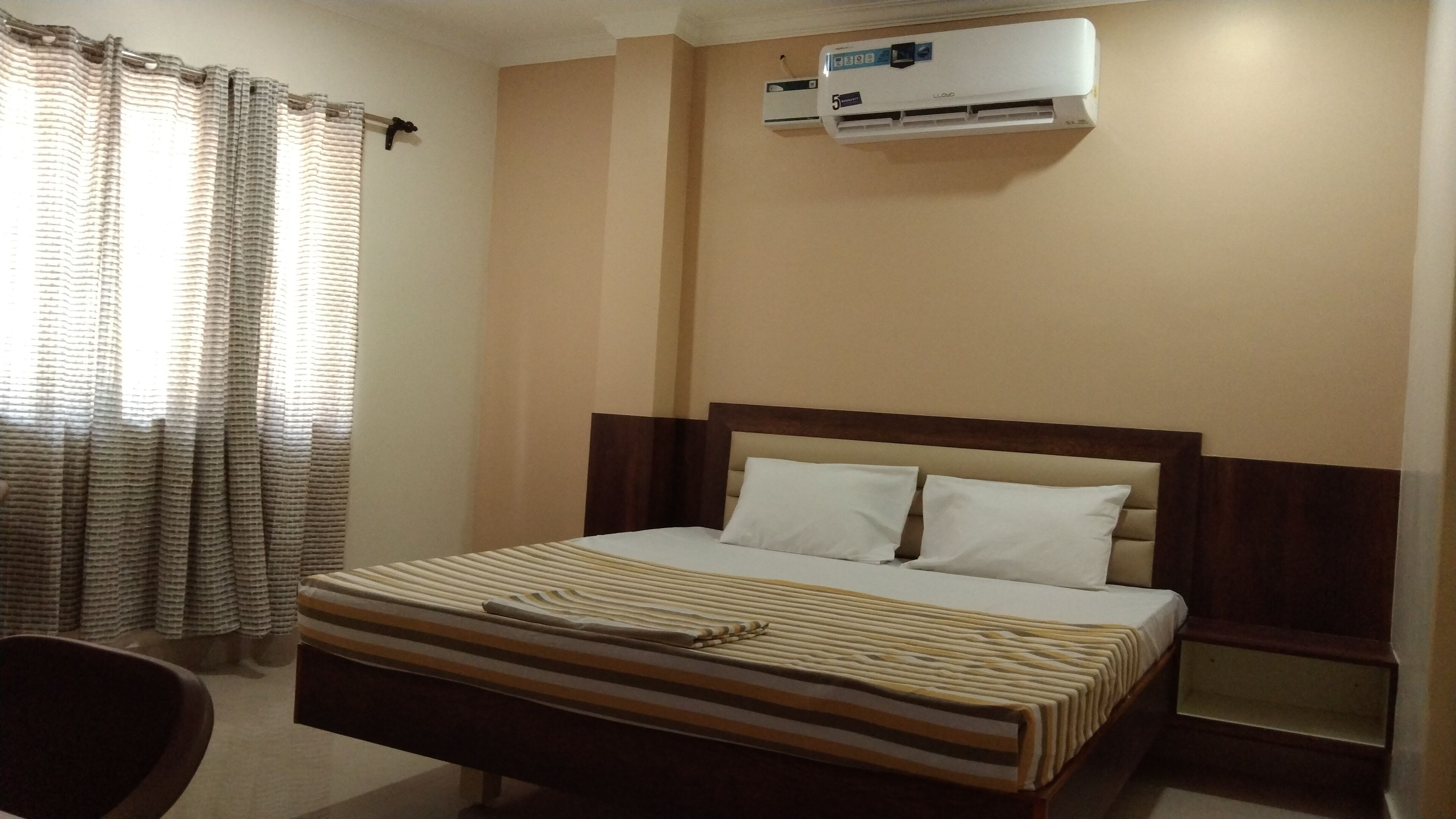 Une chambre d’hôtel avec un lit, une chaise, un appareil de climatisation et une fenêtre avec des rideaux.