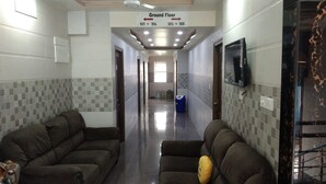 Um corredor com dois sofás, uma televisão fixada na parede e uma placa indicando os quartos 101 a 106.