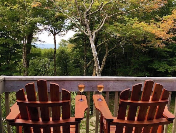 Dos sillas Adirondack de madera en una terraza de madera con vista a un área boscosa.
