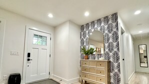 A hallway with a white door, a wooden dresser with drawers, a potted plant, and a patterned wall.