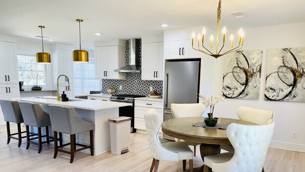 A modern kitchen with white cabinetry, a central island, and a dining area with a round table and white chairs.