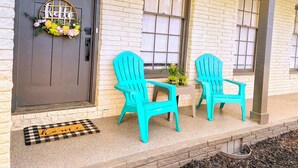 A house with a grey door, a welcome mat, and two turquoise Adirondack chairs on the porch.