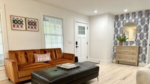 A living room with a brown leather sofa, a black leather ottoman, and a wooden dresser with a mirror.