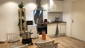 Une cuisine moderne avec des armoires blanches, une hotte en acier inoxydable et un coin repas comprenant une table et des chaises en bois.