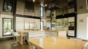 A modern kitchen with white cabinetry, a large island, and a dining area with a wooden table and bar stools. - Spacious house with heated pool 7 minutes from the sea. (Les sables d olonne)