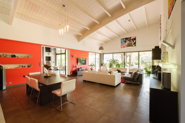 Amplia sala de estar con techos altos, comedor con mesa larga y zona de estar con sofás.