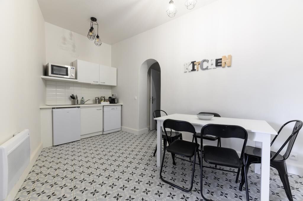 Une cuisine compacte avec des meubles blancs, un four à micro-ondes et un coin repas comprenant une table blanche et des chaises noires.