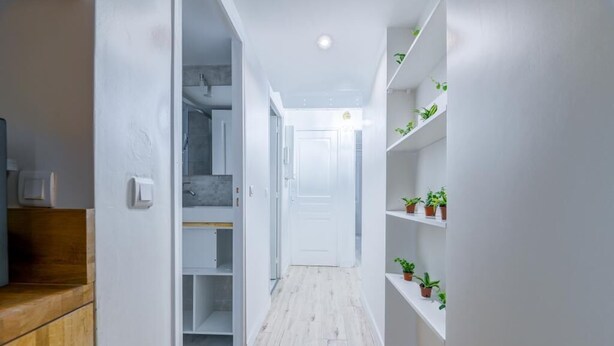 A narrow hallway with a wooden floor, white walls, and shelves with potted plants. - Villa Poncelet - Suite Coco mademoiselle, 2 Bdrs, Champs Elysées, A/C, Prime Loc (Paris-17E-Arrondissement)
