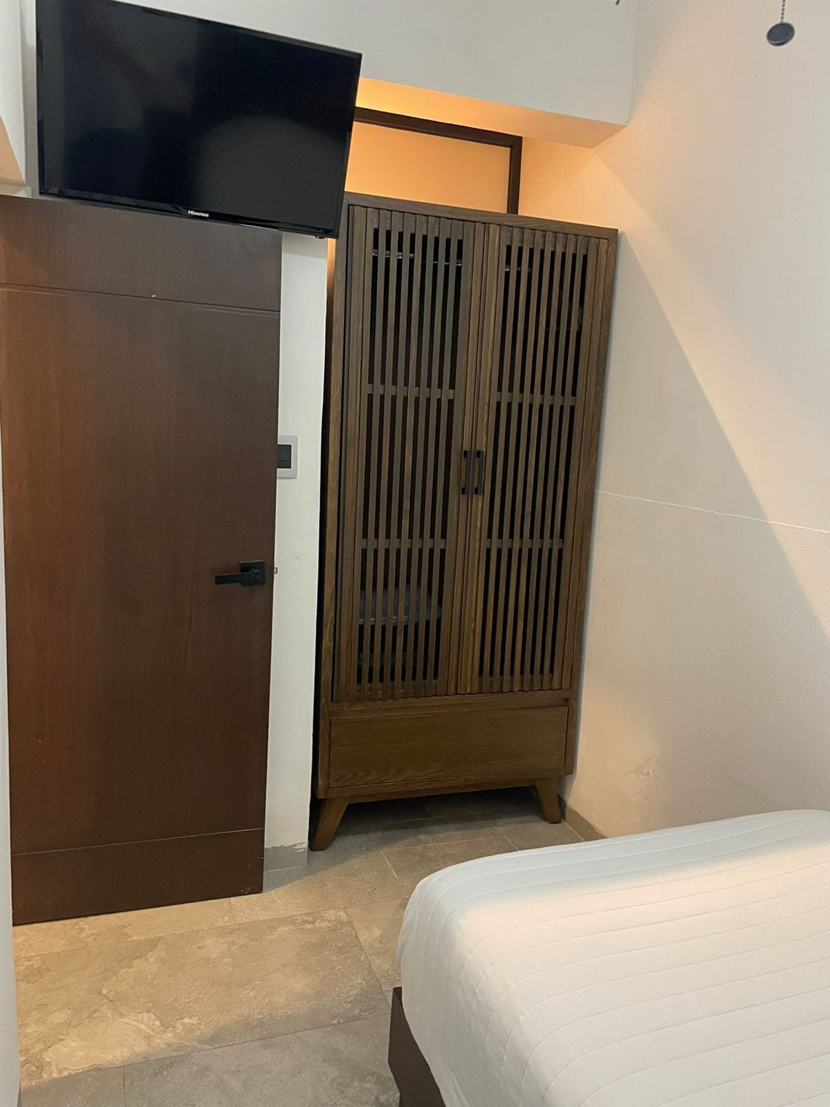 A bedroom with a bed, a wardrobe, and a television mounted on the wall.
