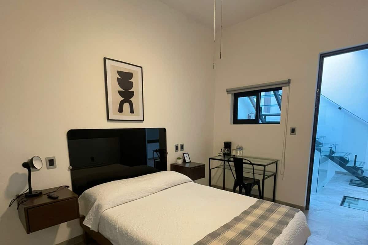 A bedroom with a bed, bedside table, desk, chair, and a window.