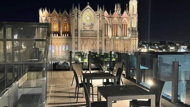 En tagterrasse med borde og stole, med udsigt over en historisk bygning i gotisk stil.