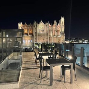 A rooftop terrace with tables and chairs, overlooking a historic building with Gothic architecture. - La Casa Mia Leon (León)