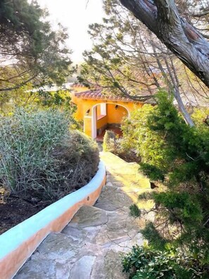 A stone pathway leading to a small, yellow building with a tiled roof, surrounded by greenery and trees. - Villa Di Canio, private pool, Wi-Fi, and Netflix (Stintino, Italia)