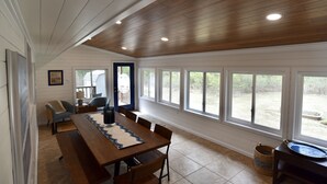 Ein Essbereich mit einem langen Holztisch, Stühlen und Blick ins Freie durch große Fenster.