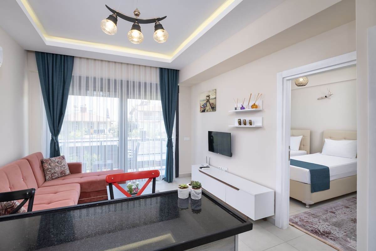 Ein modernes Hotelzimmer mit Sofa, Esstisch, Fernseher, Bett und einem kleinen Balkon.