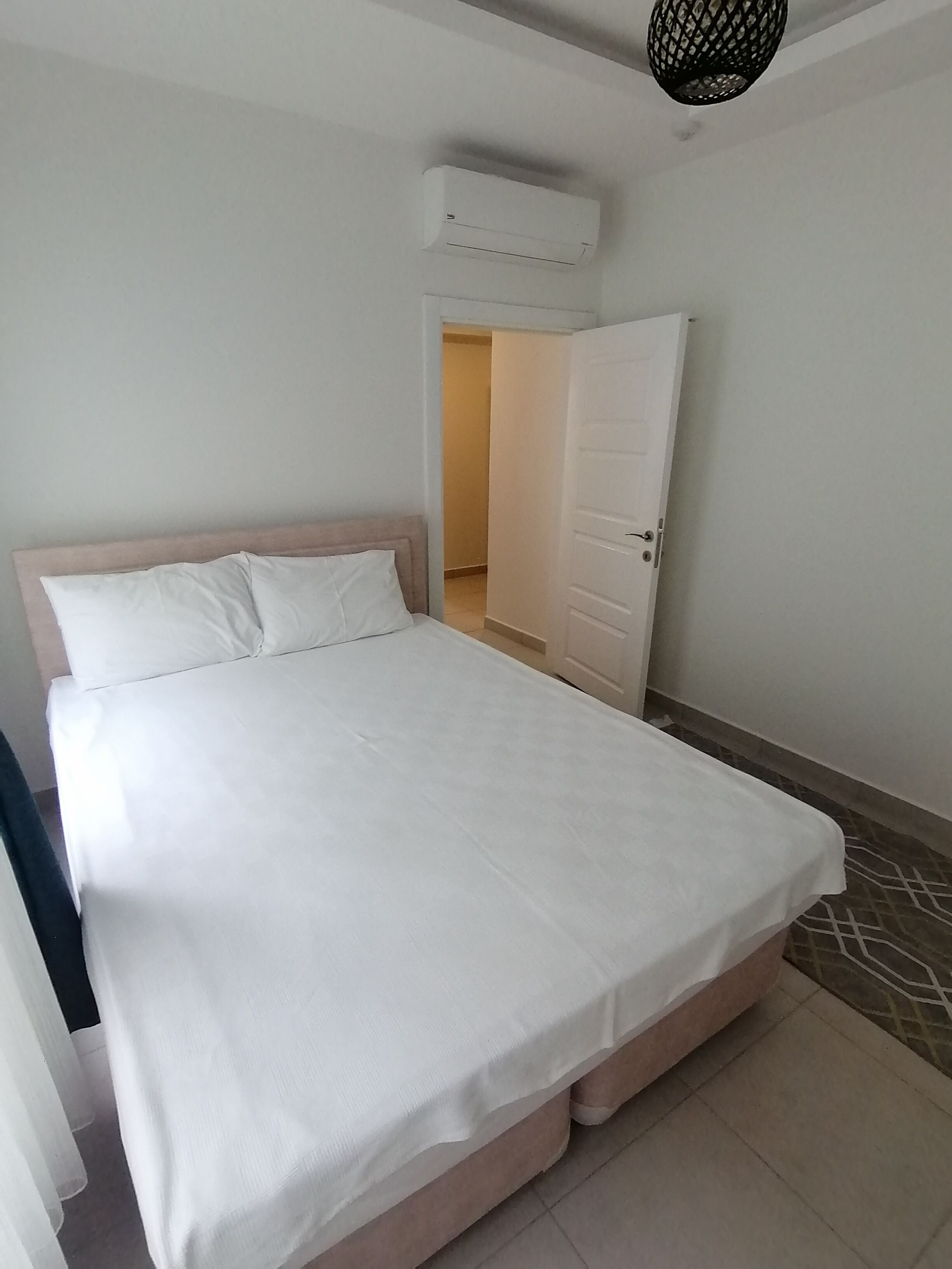 A bedroom with a bed, an air conditioning unit, a door, and a patterned floor.