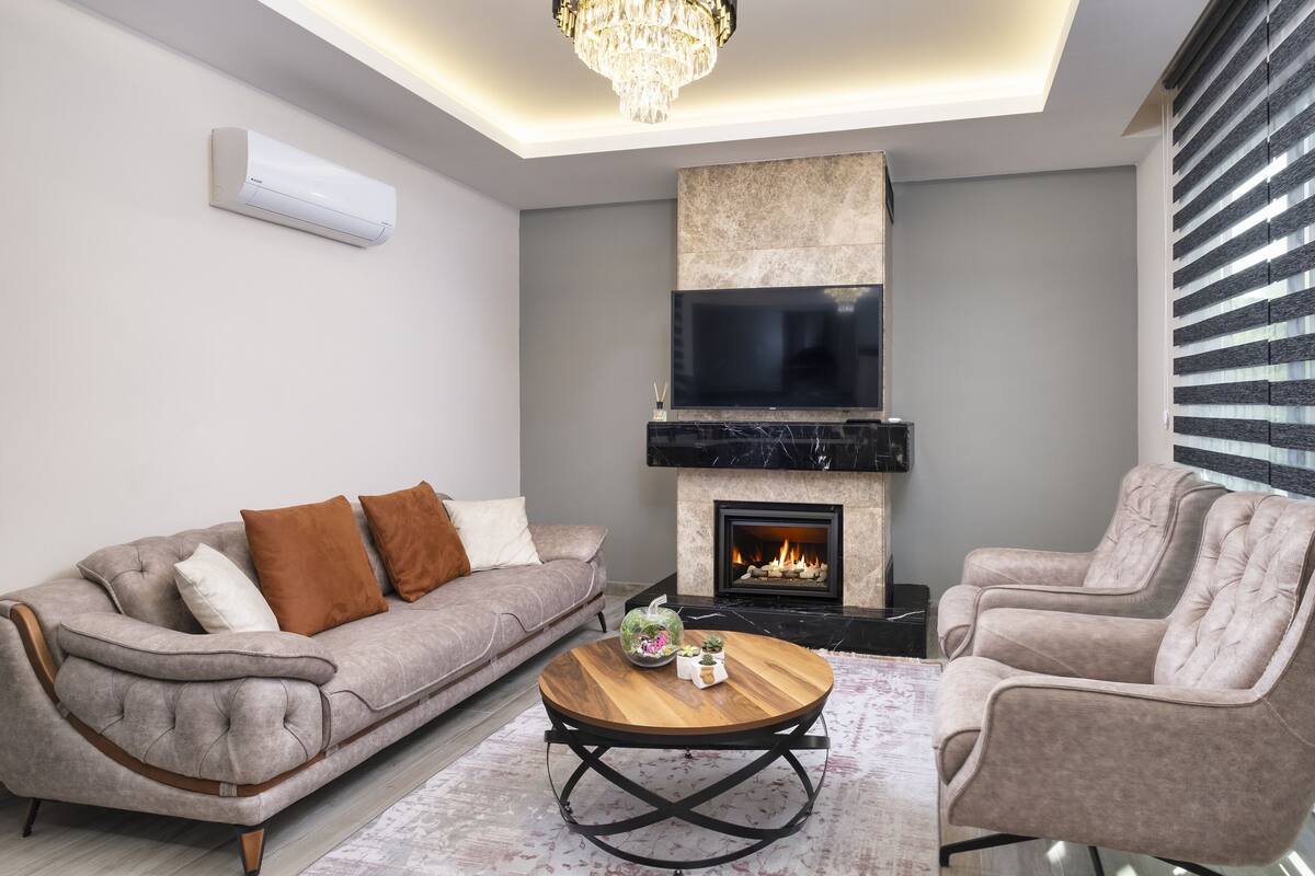 Ein modernes Wohnzimmer mit Sofa, Sessel und Couchtisch, inklusive Kamin und einem an der Wand montierten Fernseher.