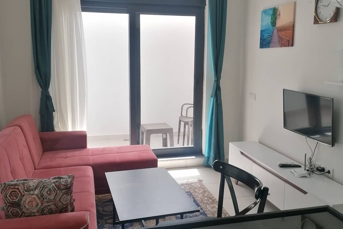 Ein Wohnzimmer mit einem roten Sofa, einem schwarzen Couchtisch, einem Fernseher und einem Balkon mit Blick.