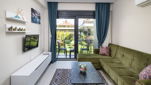 Un soggiorno moderno con un divano verde, una televisione a schermo piatto e un balcone con mobili da esterno.
