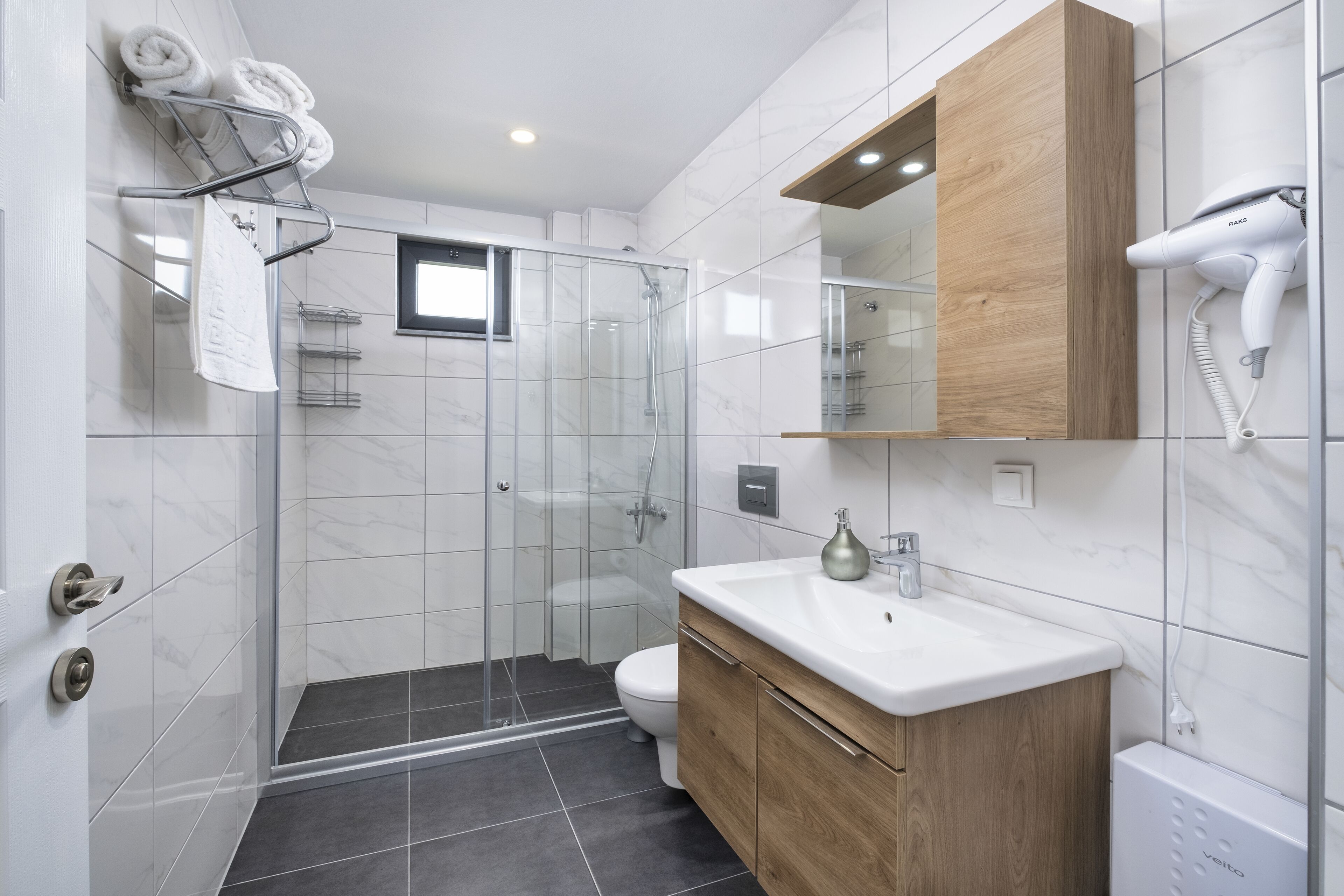 Un baño moderno con cabina de ducha de vidrio, lavabo blanco y tocador de madera.
