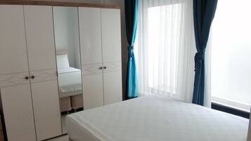 Ein Schlafzimmer mit Bett, Kleiderschrank, einer Pendelleuchte und einem Fenster mit Vorhängen.