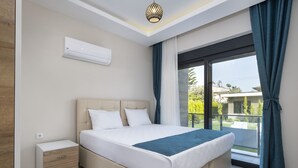 Una camera da letto moderna con un letto grande, un comodino, un condizionatore d'aria e vista all'esterno tramite una porta scorrevole in vetro.