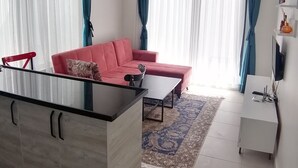 Un soggiorno moderno con un divano rosso, un tavolino da caffè con piano in vetro e un armadietto bianco.
