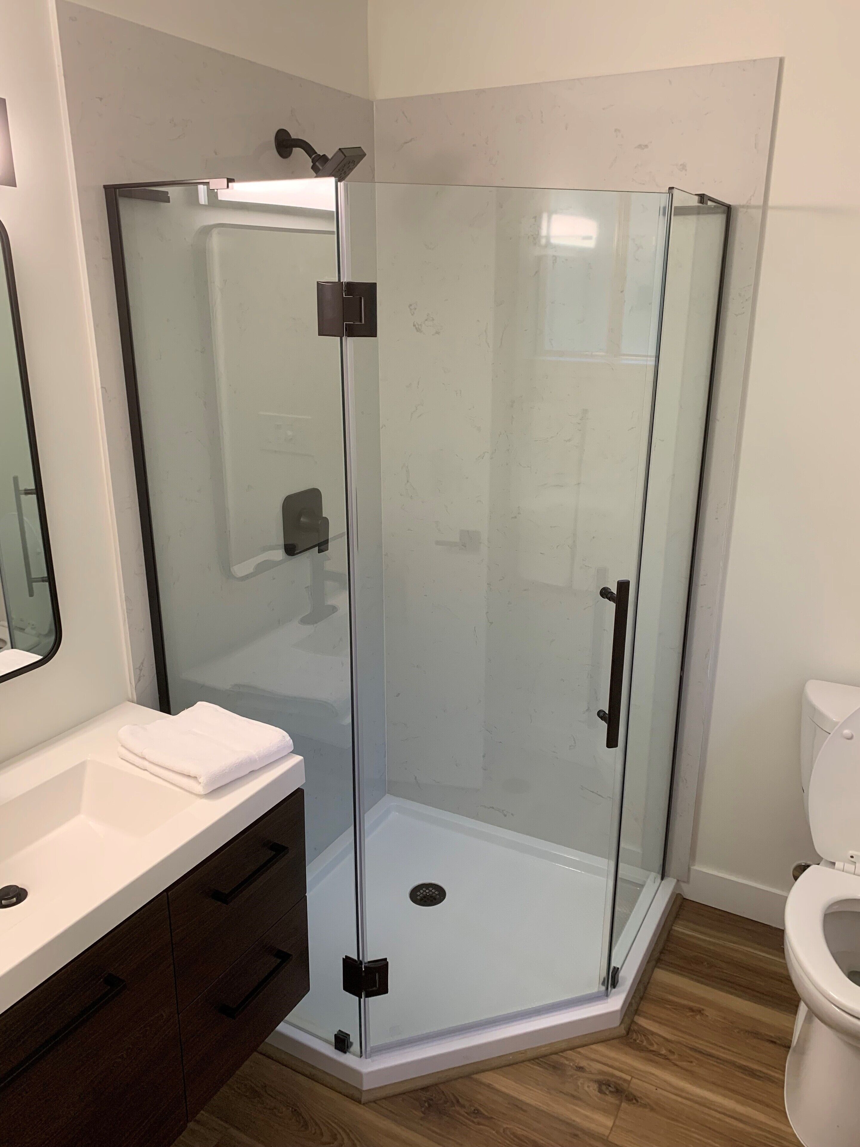Un baño moderno con ducha envuelta en vidrio, un lavabo blanco con espejo y un inodoro.