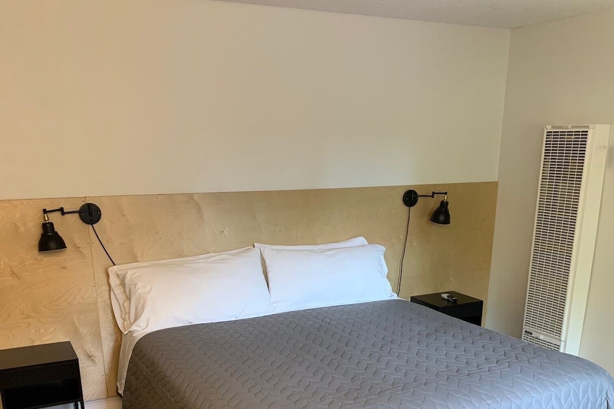 Ein Schlafzimmer mit einem Bett, zwei Nachttischen, einer Wandlampe und einem Lüftungsgitter.