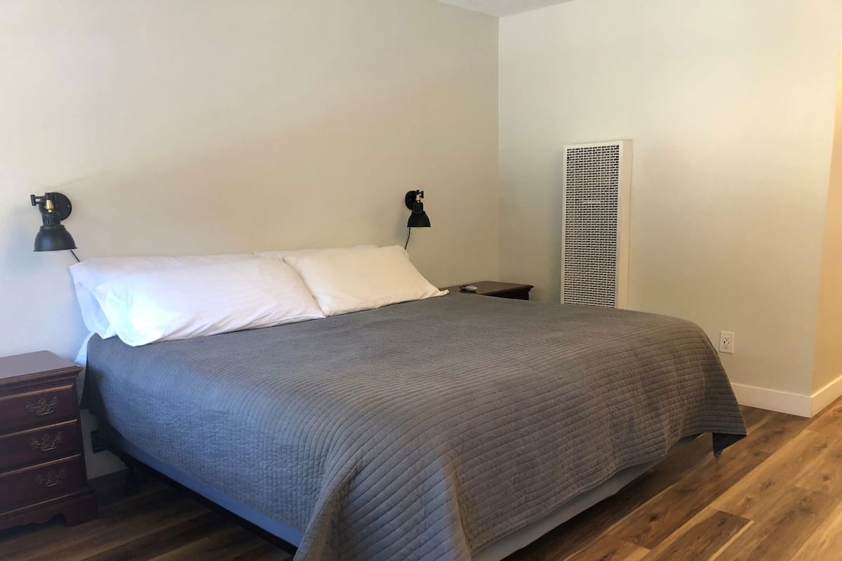 Ein Schlafzimmer mit einem Bett, zwei Nachttischlampen, einem Nachttisch, einem Heizgerät und Holzboden.