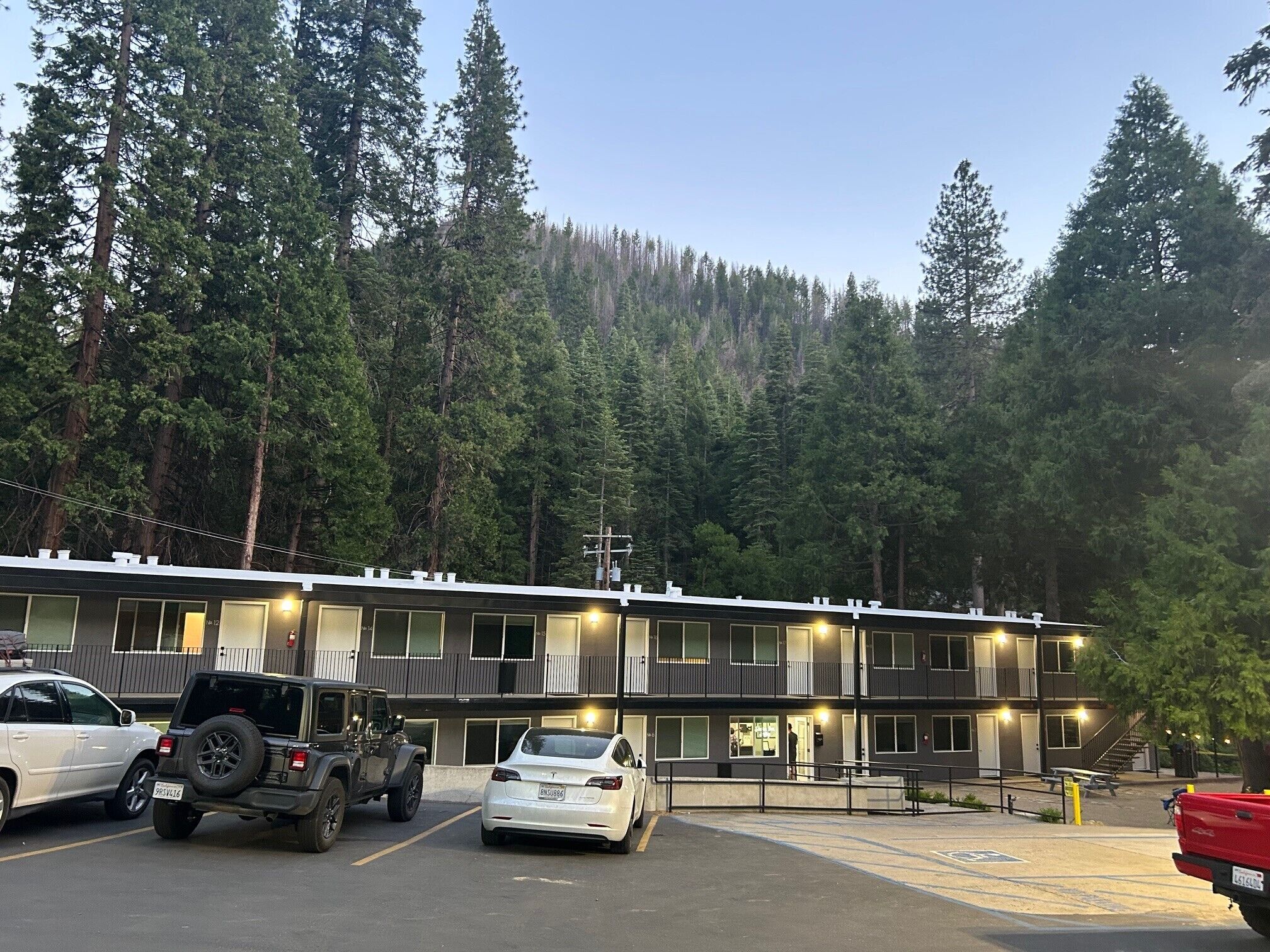 A multi-story motel with a parking lot, surrounded by dense forest.