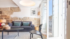 A modern living room with a stone wall, a grey sofa, a round table, and a chair.
