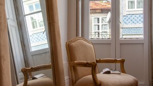 Una habitación con dos sillas de madera, un ventanal con contraventanas azules estampadas y vistas a un edificio con tejado de azulejos.