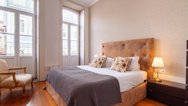 Una habitación de hotel con una cama grande, una silla de madera, una mesita de noche y una lámpara.