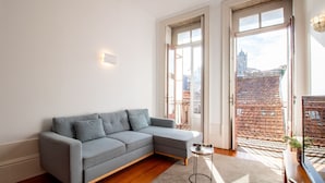 Una sala de estar moderna con un sofá seccional gris, una mesita auxiliar y vistas a un paisaje urbano a través de amplios ventanales.