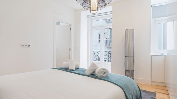 A bedroom with a large bed, a window, a door, and a tall floor lamp. - Lusitano's 2BDR Apartment in Alfama by LovelyStay (Lisboa)