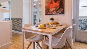 A dining area with a wooden table, white chairs, and a breakfast setting including croissants and orange juice. - Lusitano's 2BDR Apartment in Alfama by LovelyStay (Lisboa)