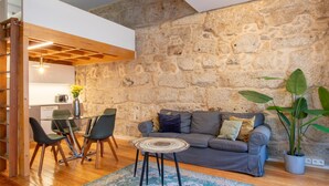 Una sala acogedora con una pared de piedra, un sofá gris, una mesa de centro y una mesa de comedor con sillas.