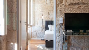Un dormitorio con pared de piedra, una cama, un televisor y una mesita de noche.