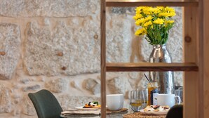 Un comedor con pared de piedra, una mesa dispuesta con un plato de comida, una taza y un vaso de agua.