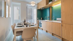 Eine moderne Küche mit Holzausstattung, einer türkisblauen Spritzschutzwand und einem Essbereich mit Tisch für vier Personen.