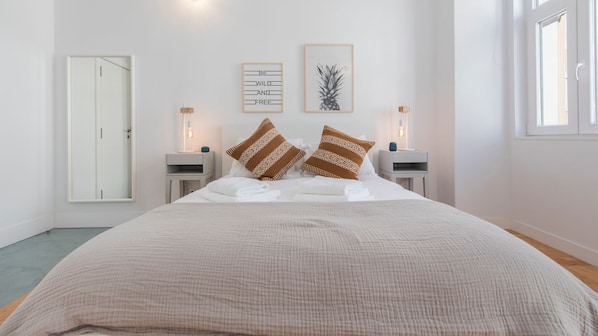 A bedroom with a large bed, two bedside tables with lamps, a door, and a framed picture on the wall.