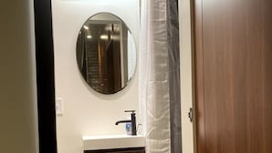 A bathroom with a wooden vanity, a round mirror, a white shower curtain, and a light fixture above the mirror.