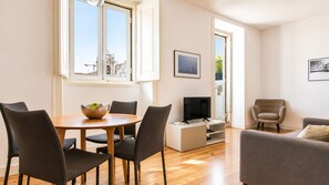 A modern living room with a dining area, a flat-screen TV, and a window with a view of buildings.