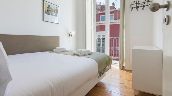 A bedroom with a bed, a bedside table, a door, and a view of the outside.