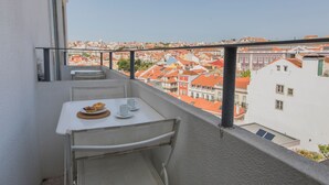 Un balcon avec une table et des chaises, donnant sur un paysage urbain avec des bâtiments aux toits rouges.