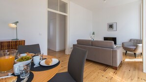 Un salon moderne avec un canapé, des fauteuils, une table à manger où sont disposés des aliments pour le petit-déjeuner et un téléviseur.
