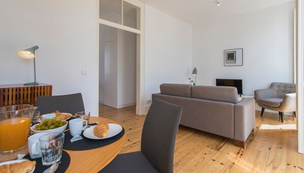 A modern living room with a sofa, chairs, a dining table with breakfast items, and a TV.