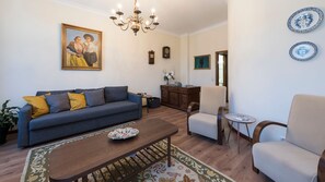 Una sala de estar con un sofá, sillones, una mesita de centro, una araña y un cuadro en la pared.