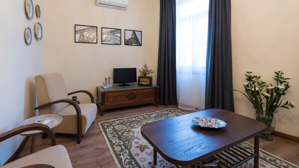 Una sala de estar con un sofá, una mesa de centro de madera, un televisor sobre un mueble de madera y un jarrón decorativo con flores.